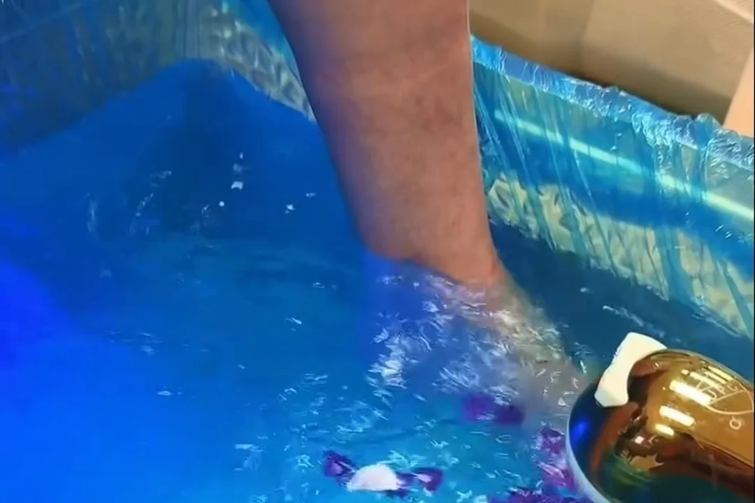 Feet soaking in bright blue water with purple flower petals in a lined pedicure basin